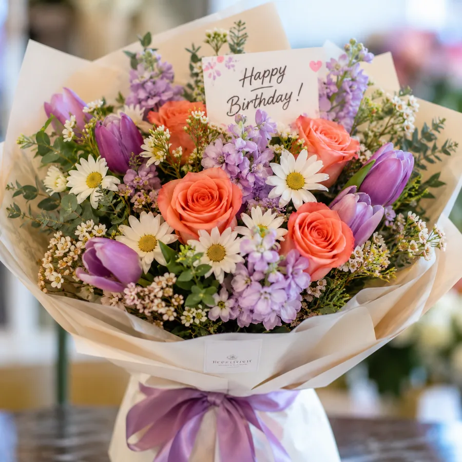 Birthday bouquet of coral roses, purple tulips, white daisies and lilac stock flowers